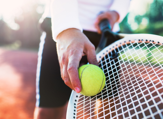 Close up of tennis racquet with hand holding tennis ball
